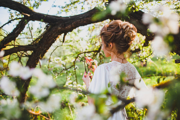 Young bride with blond hair posing at the background of spring orchard - Foto, immagini