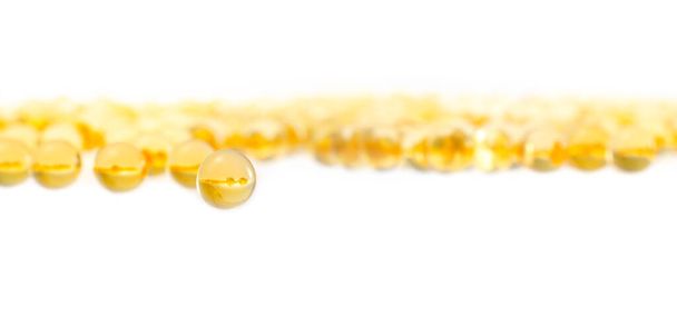 plenty scattered yellow transparent capsule fish oil or vitamin E in gelatin sheath, close up on white background - Foto, afbeelding