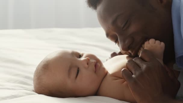 Close up of happy smiling african american man enjoying his fatherhood, embracing and playing with his newborn baby - Felvétel, videó