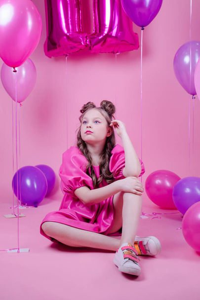 modelo morena atractiva chica con maquillaje rosa y en vestido de cuero rosa cerca de globos de colores sobre fondo rosado. Concepto de alegría, fiesta, cumpleaños - Foto, imagen