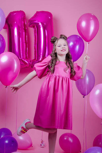 sweet brunette girl with pink make up and in pink leather dress. near colorful balloons in shape of number eleven. on pink background.concept of joy, party, birthday celebration - Photo, Image