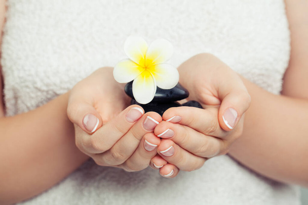 Spa-, Wellness- und Ayurveda-Konzept. Weibliche Hände mit schwarzen Massagesteinen und Blume - Foto, Bild