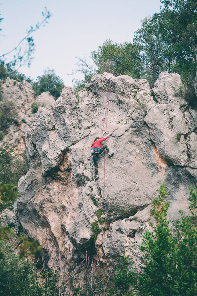Dziewczyna wspina się na skałę. Sportowiec trenuje w przyrodzie. Kobieta pokonuje trudną trasę wspinaczkową. Silny alpinista. Ekstremalne hobby. - Zdjęcie, obraz