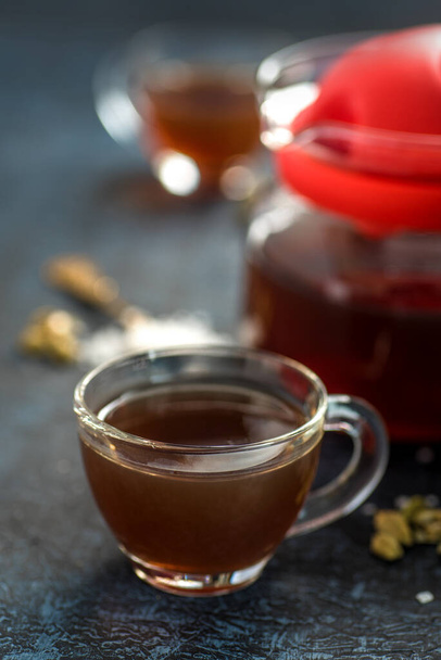 A cup of tea and cardamom with sugar in a spoon on a textured background. - Foto, afbeelding