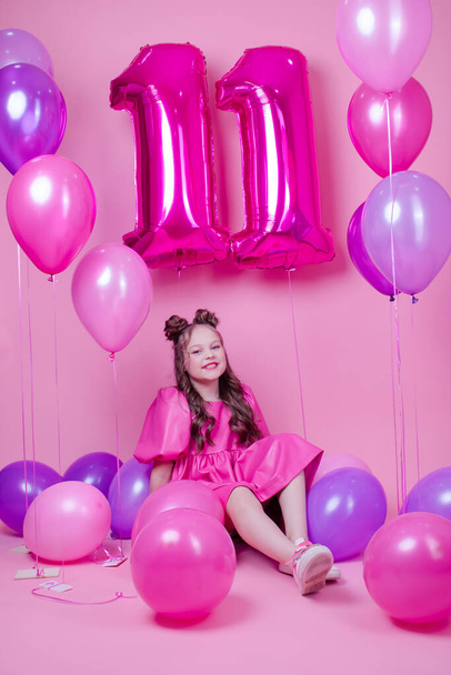 piękna dziewczyna z różowym makijażu i w różowej skórzanej sukience. blisko kolorowych balonów w kształcie jedenastki 11. na różowym tle. koncepcja obchodów urodzin - Zdjęcie, obraz