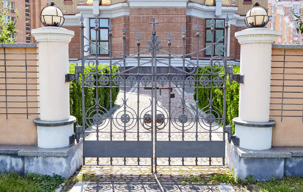 Wrought iron gates for a temple or church. Image of a Beautiful decorative cast iron wrought fence and gates with artistic forging and stone columns - Zdjęcie, obraz