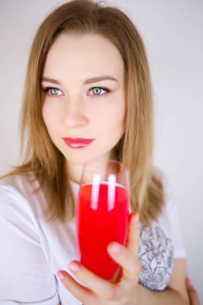 Una hermosa mujer con maquillaje, una chica sosteniendo un vaso de líquido rojo delante de ella - Foto, Imagen