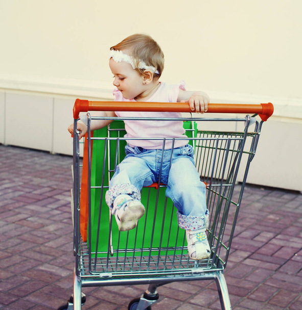 Happy baby with shopping bags sitting in a trolley cart in a city - 写真・画像