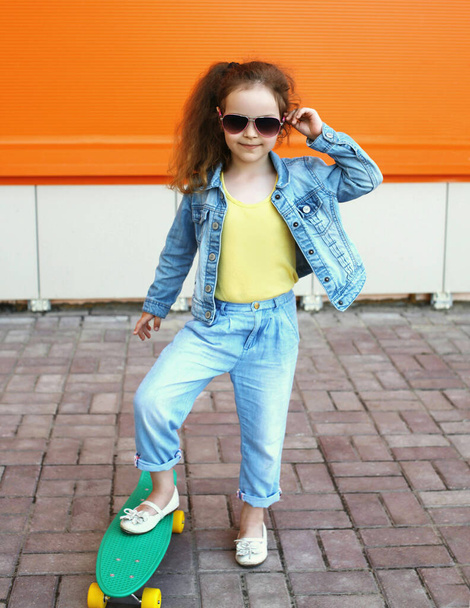 Portrait of little girl child posing with skateboard in the city on an orange background - Photo, image