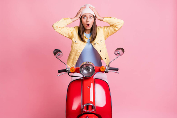 Photo of young shocked surprised girl woman hold hands head ride red motorbike isolated on pink color background - Foto, afbeelding