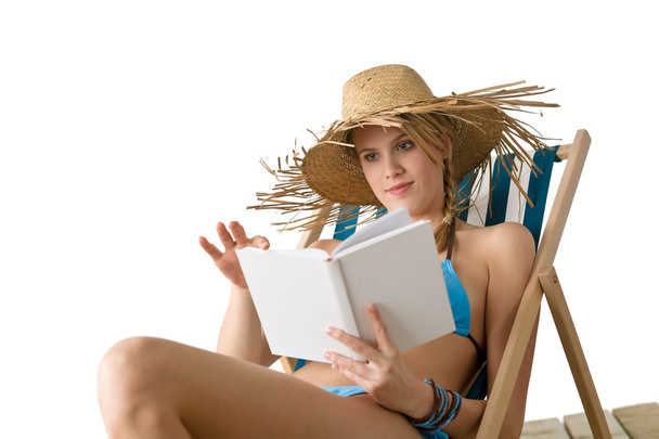 Beach - Happy young woman relax with book sitting on deck chair in bikini with straw hat - Fotó, kép
