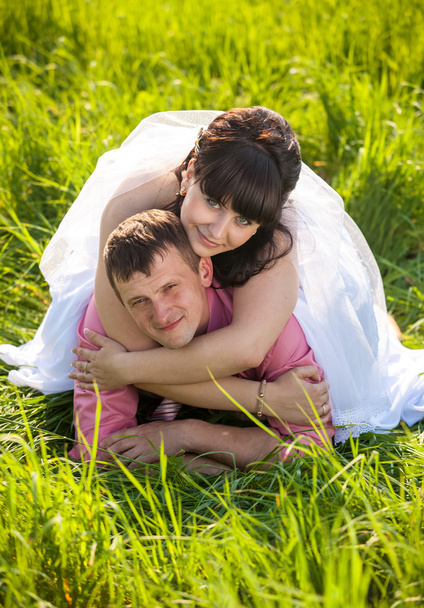 Portret van gelukkige bruid liggend op bruidegoms terug op veld - Foto, afbeelding