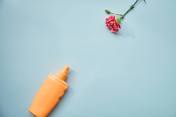 Cosmetic bottle mock up and pink delicate flower on blue background. A modern conceptual female plot. Copy space - Foto, immagini