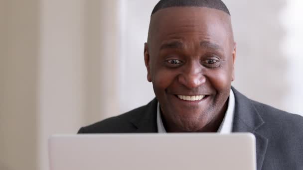 Мужской портрет африканский зрелый бизнесмен среднего возраста работодатель афро-предприниматель, глядя на ноутбук получает хорошие новости уведомление открывает глаза широко чувствовать шок победы кивает головой да делает видеозвонок - Кадры, видео
