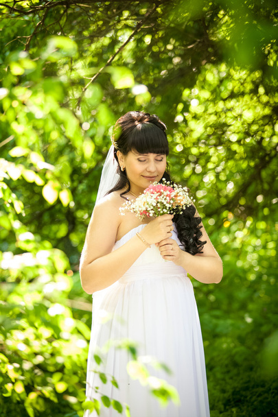 smiling cute bride smelling bouquet at park - Foto, Bild