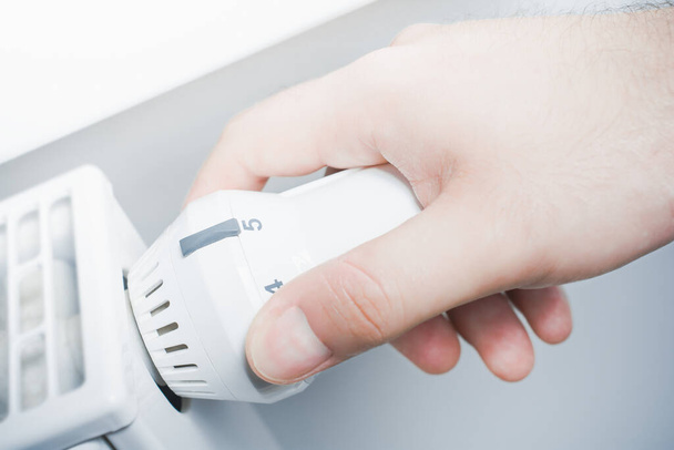 Male Hand Turns The Radiator Of A White Heater In The Living Room - Saving Energy Concept - Photo, Image