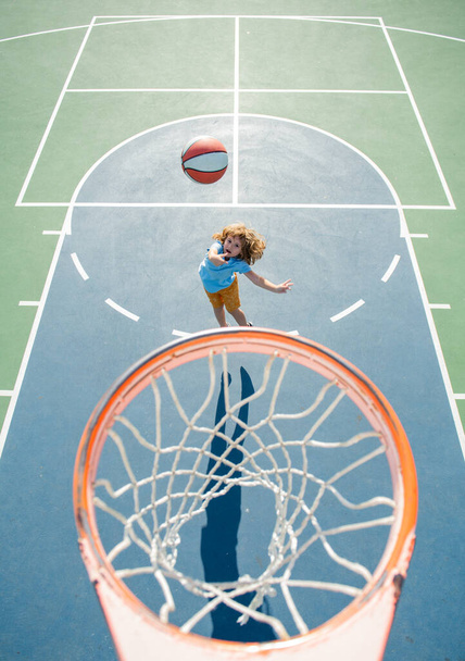 Child in basketball uniform jumping with basket ball for shot on basketball court. - Photo, Image