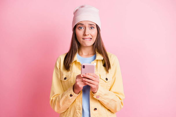 Portrait of worried young woman hold phone wear yellow jacket post mistake comment isolated on pink color background - Photo, image