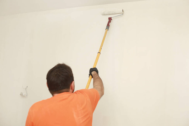 Male painting wall with paint roller. Painting apartment, renovating with white color paint. Room renovations at house - 写真・画像