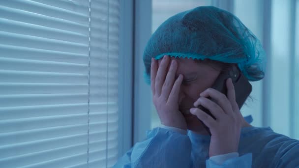 Verzweifelte Frau, die nach einem Unfall mit Gesichtsverletzungen auf ihren Krankenhausbesuch wartet, telefoniert weinend und überbringt der Familie, die am Fenster in der Notaufnahme steht, schlechte Nachrichten. Aufruf zur Versicherung - Filmmaterial, Video