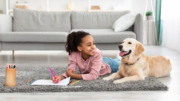 Young afro girl drawing with dog at home - Foto, imagen