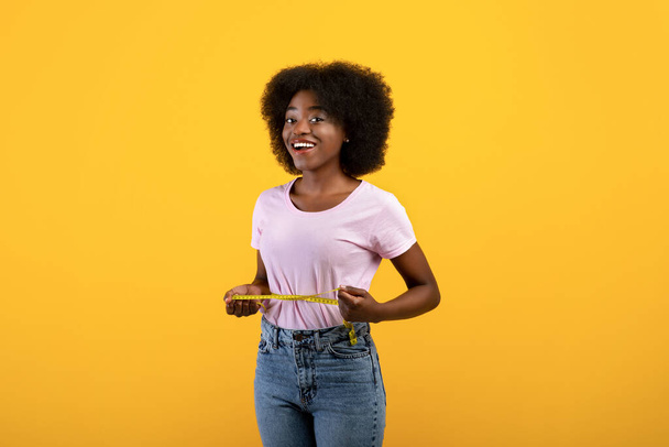 Koncepcja odchudzania. Afroamerykanka Fit mierzy talię taśmą na żółtym tle studia - Zdjęcie, obraz