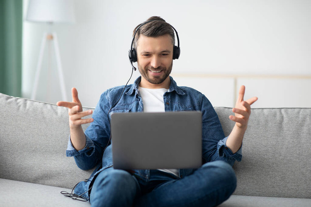 Positive man having video conference, using headset and laptop - Photo, image