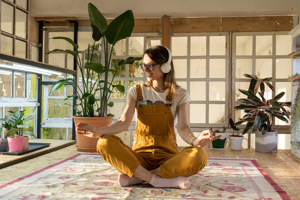 Fiatal kertésznő meditál. Gyönyörű nő kezeslábasban és fejhallgatóval pihenni tanulni vagy dolgozni - Fotó, kép