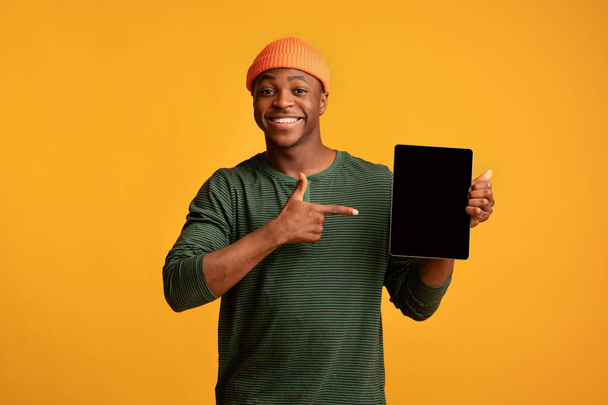 Radosny czarny facet trzymając i wskazując na tablecie cyfrowym z pustym ekranem - Zdjęcie, obraz