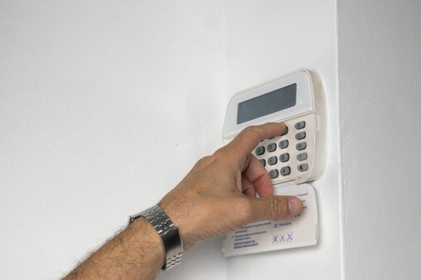 Alarm keypad with one hand by plugging it in on the white wall - Photo, Image