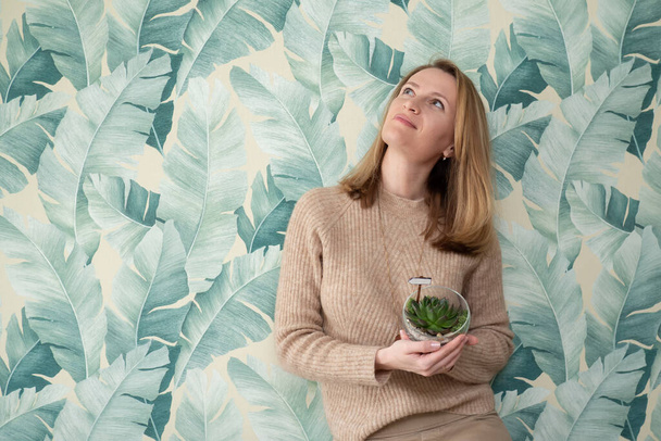 Woman holding mini succulents in pot on green banana leaves wallpaper background. Dreams and longing for travel in nature. Love for plants. Indoor eco friendly gardening - Φωτογραφία, εικόνα