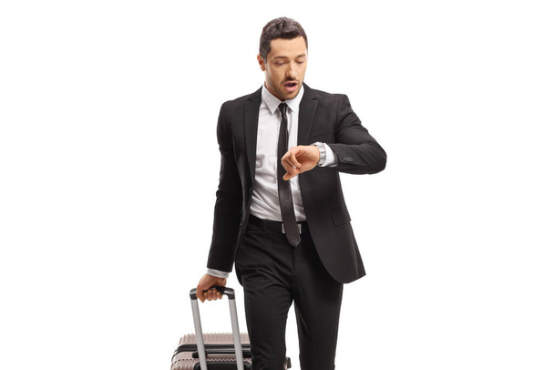Young businessman with a suitcase going on a business trip and looking at his watch isolated on white background - 写真・画像