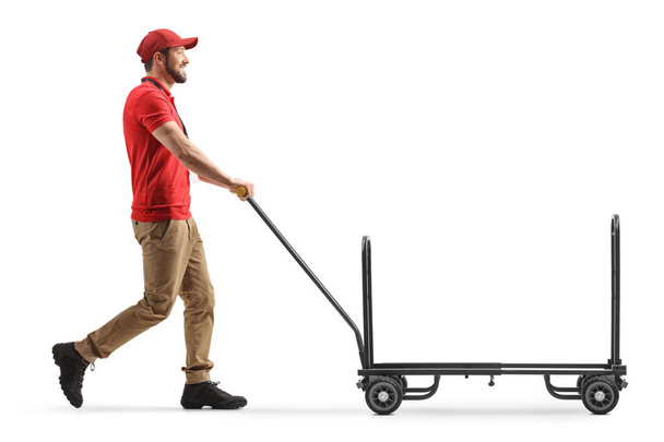 Delivery worker pushing an empty hand truck isolated on white background - 写真・画像
