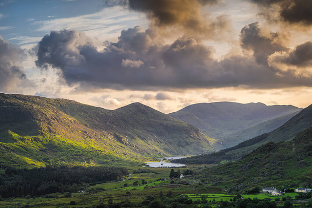 Piccolo cottage o villaggio nella Black Valley. MacGillycuddys Reeks montagne illuminate dalla luce del sole e dal cielo drammatico al tramonto, Ring of Kerry, Irlanda - Foto, immagini
