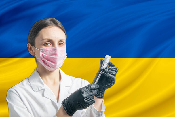 女医はウクライナの国旗を背景に予防接種を準備する。予防接種の概念｜ウクライナ. - 写真・画像