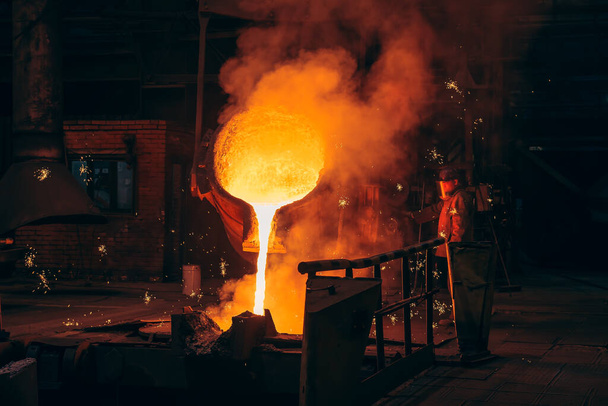 Metallurgische installatie, warm vloeibaar metaal dat in speciale vorm in gieterij met werknemer wordt gegoten - Foto, afbeelding