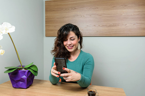Smiling, Brazilian woman, sitting and interacting with her smartphone. - Φωτογραφία, εικόνα