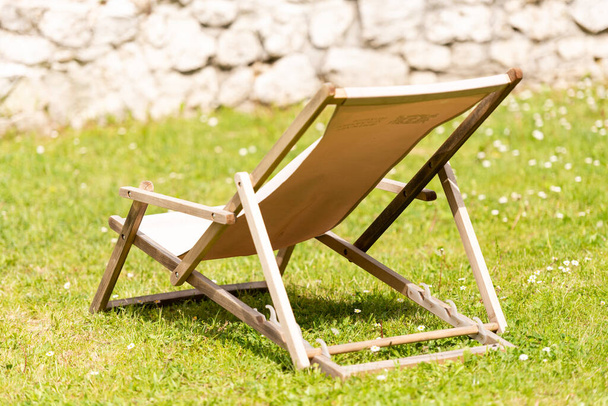 Sun lounger on the grass under the sun. A place for sunbathing. Wooden chair with fabric material. - Foto, imagen