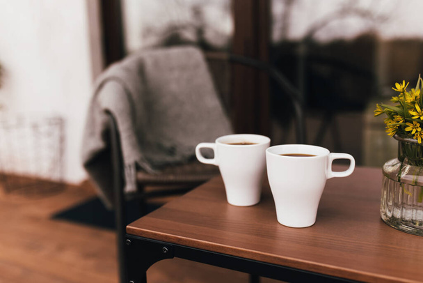 木製の茶色のテラスのテーブルの上のコーヒーの2つのカップは、背景がぼやけて日没中に。リラクゼーション、静かな田舎のサイドライフコンセプト。素敵なカップルの夜 - 写真・画像