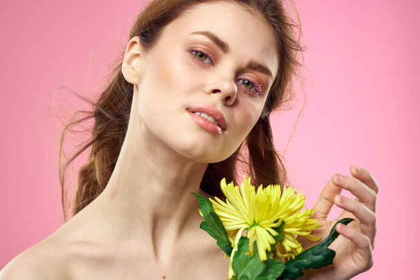 Hermosa mujer con hombros desnudos y una flor amarilla en sus manos sobre un fondo rosa - Foto, imagen