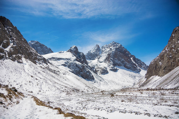 Idylliczny zimowy krajobraz ze szlakiem turystycznym w górach. Skały, śnieg i kamienie w górskiej dolinie. Panorama gór. - Zdjęcie, obraz