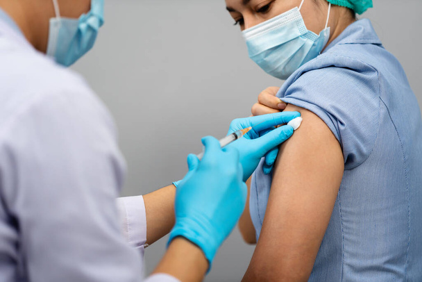 Arzt mit Spritze und Verwendung von Baumwolle vor der Injektion an Krankenschwester oder medizinisches Fachpersonal in einer Maske. Covid-19 oder Coronavirus-Impfstoff - Foto, Bild