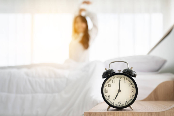 Buenos días, nuevo día. despertador despertador y mujer sentado cuerpo estirar en la cama al lado de la ventana en el dormitorio - Foto, imagen