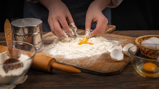 Women's hands, flour and dough. A woman, in an apron prepares dough for homemade baking, a rustic home cozy atmosphere, a dark background with unusual lighting. - Photo, Image