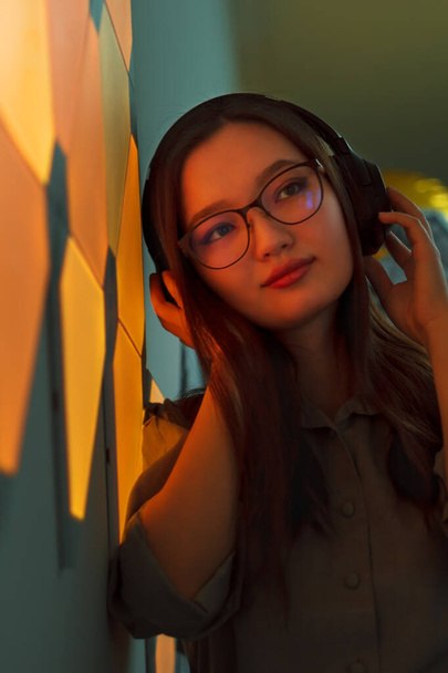 Young smiling woman with headphones in yellow neon light listen to music, nightclub futuristic neon of electronic sound - Fotoğraf, Görsel
