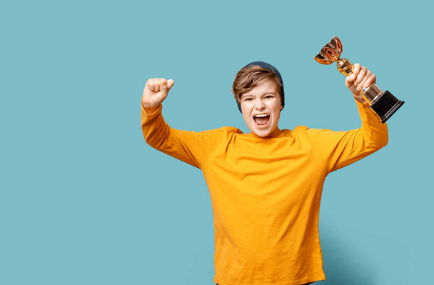 Caucasian teen school boy shouting happily and holds a trophy. Winner. Success and achievement concept. Blue banner with copy space. edgeless - Foto, Imagem