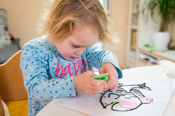 Cute girl drawing a fish using glass colors at home. - Фото, изображение