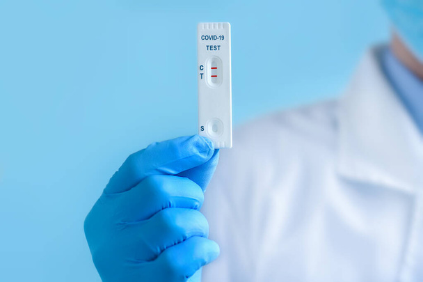 A doctor or nurse wearing a protective mask and gloves shows a rapid laboratory test for COVID-19 to detect IgM and IgG antibodies to the new coronavirus. The test shows a positive result. Copy space - Foto, immagini