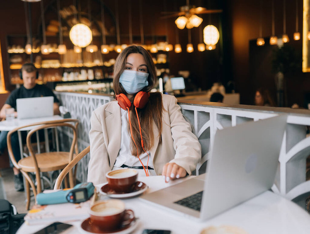 Une fille assise dans un café avec un casque. Éclosion de coronavirus. - Photo, image