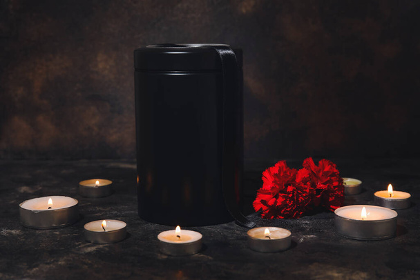 Leichenurne mit Nelkenblumen und Kerzen auf dunklem Hintergrund - Foto, Bild